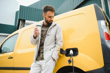 Yakışıklı adam elektrikli araba şarj ederken kahve içme.
