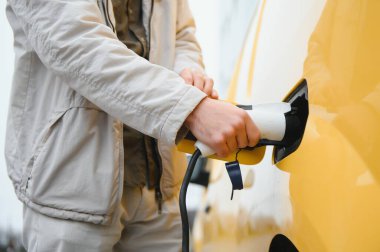 Şık bir adam şarj kablosunu elektrikli arabanın prizine yerleştirir..