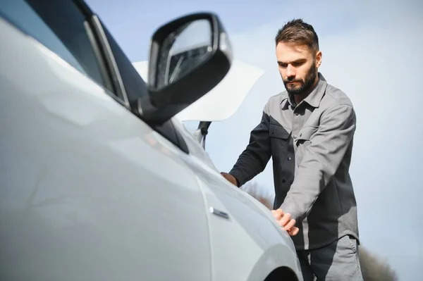 Young upset casual man trying to fix his broken car outdoors. Man waiting for towing service for help car accident on the road. Roadside assistance concept