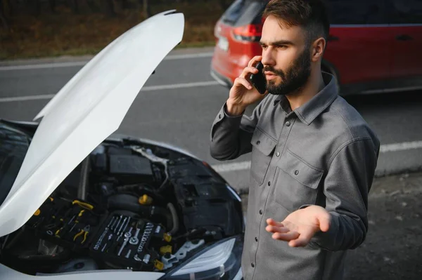 Man use a cellphone call garage in front of the open hood of a broken car on the road in the forest. Car breakdown concept