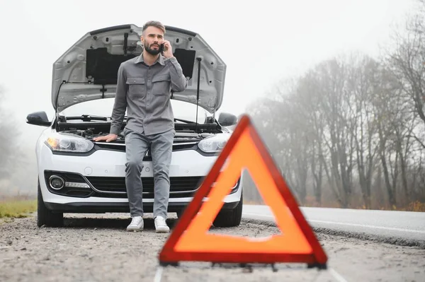 Man use a cellphone call garage in front of the open hood of a broken car on the road in the forest. Car breakdown concept