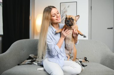 Güzel kızıl saçlı kadın kanepede oturmuş köpeğe gülüyor ve sarılıyor..