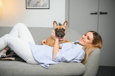 Güzel kızıl saçlı kadın kanepede oturmuş köpeğe gülüyor ve sarılıyor..