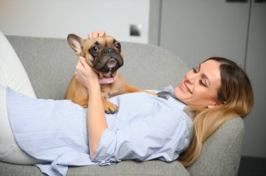 Güzel kızıl saçlı kadın kanepede oturmuş köpeğe gülüyor ve sarılıyor..