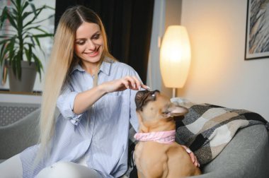 Güzel kızıl saçlı kadın kanepede oturmuş köpeğe gülüyor ve sarılıyor..