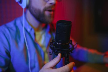 Genç adam küçük yayın stüdyosunda mikrofon kullanarak podcast yapıyor ya da kaydediyor. İçerik oluşturucu