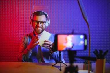 Erkek teknoloji blogcusu video blogu ya da yeni akıllı telefonun video blogu eleştirisini kaydediyor, bunu ev stüdyodaki kamerada gösteriyor. Blog yazma, ev işleri konsepti. Seçici odaklanma. Web Afişi.