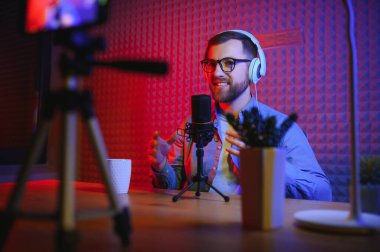 Stüdyoda canlı yayın yapmak için akıllı telefon kullanıyor. Sosyal medya yayıncılığı kariyeri için cep telefonu, mikrofon ve kulaklık kullanan blog yazarı