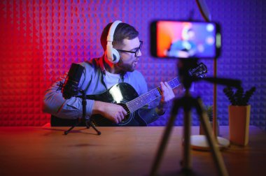 Sıradan giyinen sakallı genç bir tarz sahibi ya da akıllı telefon kamerasının önünde gitar çalan bir müzik öğretmeni. Online gitar eğitimi ya da vokal dersi.