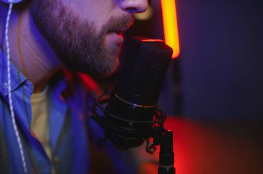 Genç adam küçük yayın stüdyosunda mikrofon kullanarak podcast yapıyor ya da kaydediyor. İçerik oluşturucu