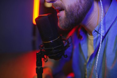 Genç adam küçük yayın stüdyosunda mikrofon kullanarak podcast yapıyor ya da kaydediyor. İçerik oluşturucu