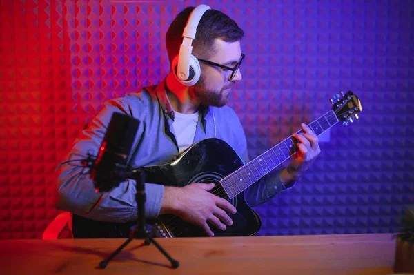 stock image Close up man in headphones playing guitar and singing, recording on smartphone, musician artist recording new song video for social network, blogger or music teacher shooting course in home studio.