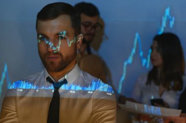 Ticaret öğretmenliği. Erkek lider çalışanlarla konuşuyor. Borsa şirketinin projektörüyle ilgili planı gösteriyor.