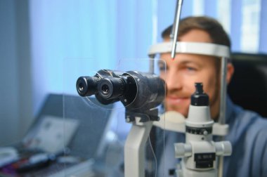 Yetişkin bir adamın dürbün kesme lambasıyla görme testi. Erkek gözünün retinasını yakından kontrol ediyorum. Oftalmoloji Kliniği.
