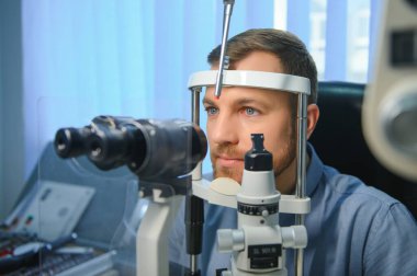 Göz doktorunda göz muayenesi yaptıran yakışıklı bir adam. Erkek gözünün retinasını yakından kontrol ediyorum..
