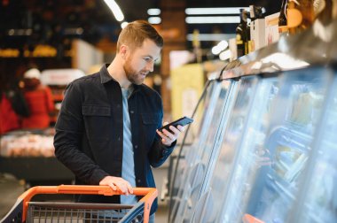Yakışıklı adam, modern süpermarketten ya da marketten sağlıklı yiyecek ve içecek alıyor. Yaşam tarzı ve tüketim konsepti