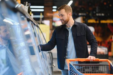 Yakışıklı adam, modern süpermarketten ya da marketten sağlıklı yiyecek ve içecek alıyor. Yaşam tarzı ve tüketim konsepti
