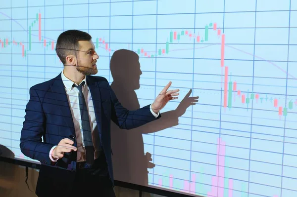 Young Businessman Explaining Graphs To His Colleagues On Projector.