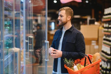 Süpermarketteki müşteri. Market alışverişi yapan bir adam, araba ile ayakta duruyor, içeride yiyecek seçiyor. Gıda mağazasından alışveriş yapan adam. Seçici Odaklanma, Boşluğu Kopyala