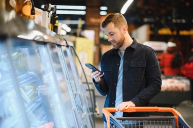 Genç adam süpermarketten alışveriş yapıyor. Arka plandaki diğer müşteriler. Tüketim kavramı