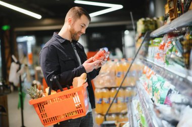 Yakışıklı adam, modern süpermarketten ya da marketten sağlıklı yiyecek ve içecek alıyor. Yaşam tarzı ve tüketim konsepti