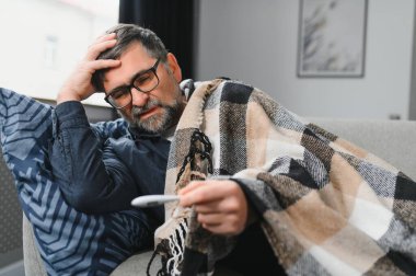 Termometre kullanan hasta kıdemli bir adam mevsimsel grip ya da soğuk algınlığı yüzünden vücut ısısını kontrol ediyor.
