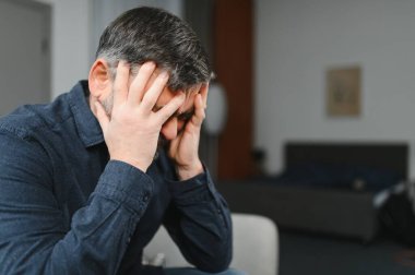 50 'li yaşlarda erkek yüzünü saklar, elleri umutsuzca bakar, yaşlı erkek kanepede oturur, arama kararının kötü hissettirdiğini düşünür, yaşlı insanların zihinsel bozuklukları, bunak hastalıkları, bunama konsepti.