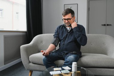 Yaşlı adam kan basıncını ölçmek için tıbbi cihaz kullanıyor..