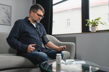 Yaşlı adam kan basıncını ölçmek için tıbbi cihaz kullanıyor..