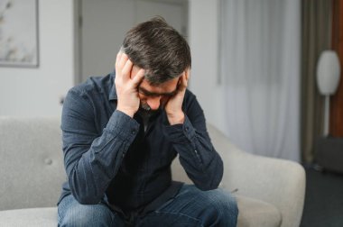 Evinde baş ağrısı çeken, şakaklarına dokunan, fotokopi çeken orta yaşlı sakallı bir adam. Migren, baş ağrısı, stres, gerilim sorunu, akşamdan kalma konsepti.