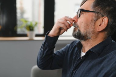 Burun spreyli bir adamın portresi. Hasta adam yatakta yatarken burun damlası kullanıyor. Alerji için tedavi kavramı mı yoksa soğuk algınlığı mı?