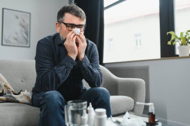 Yaşlı adam evde kağıt mendille üşütüp hapşırır..