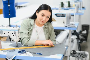 Young dressmaker woman sews clothes on working table. Smiling seamstress and her hand close up in workshop