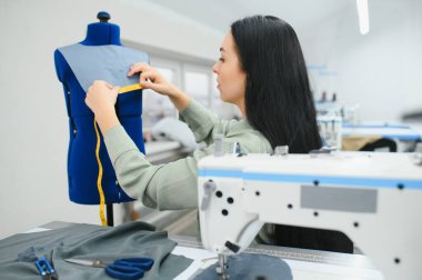 Happy female dressmaker working with sewing machine at textile factory