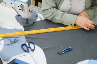 Young dressmaker woman sews clothes on working table. Smiling seamstress and her hand close up in workshop