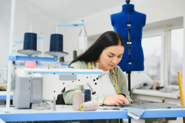 Happy female dressmaker working with sewing machine at textile factory