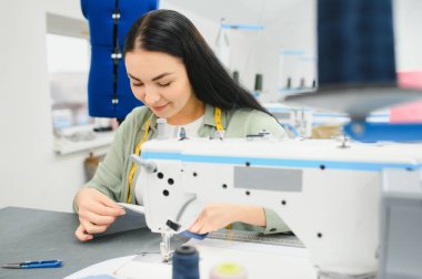 Happy female dressmaker working with sewing machine at textile factory