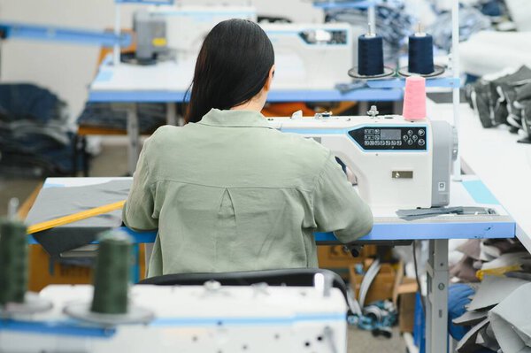 Счастливая привлекательная молодая женщина швея сидит и шьет швейную машинку в студии.