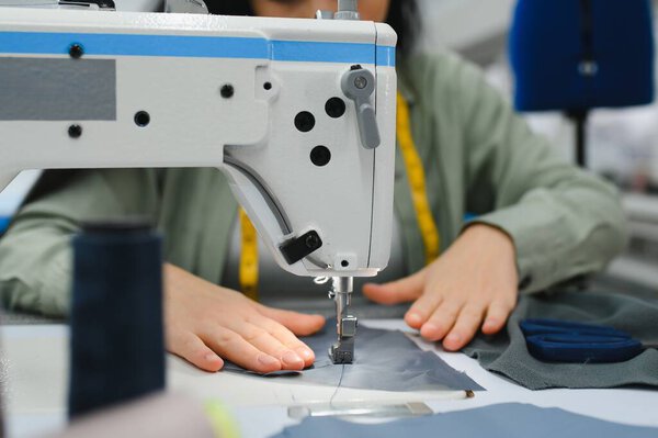 Happy female dressmaker working with sewing machine at textile factory