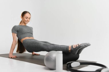 Fit young brunette pilates instructor showing different exercises on a white background a mat