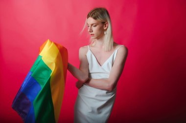 Young gay man 20s with make up wrapped in rainbow striped flag isolated on background, studio portrait. People lifestyle fashion lgbtq concept
