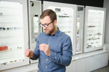 Shot of a handsome bearded man trying on new glasses at the eyewear store.Man buying glasses.Health, eyesight, vision, fashion, shopping.
