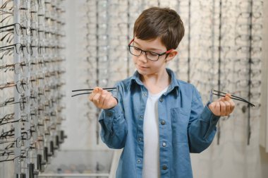Smiling boy choosing glasses in optics store, Portrait of kid wearing glasses at optical store.
