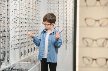 Smiling boy choosing glasses in optics store, Portrait of kid wearing glasses at optical store.