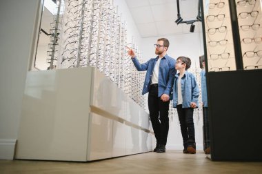 Dad and son choose new stylish glasses in an optical store. Vision care concept.