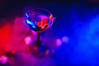 Martini glass and olives on a black background with neon lights.