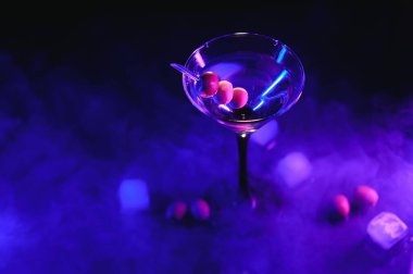 Martini glass and olives on a black background with neon lights.