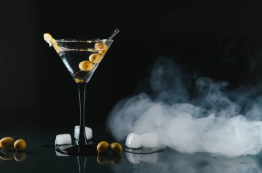 Glass of classic dry martini cocktail with olives on dark table against black background. With free space for your text.