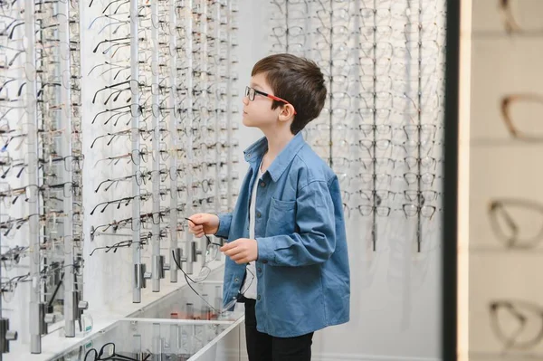 Smiling boy choosing glasses in optics store, Portrait of kid wearing glasses at optical store.