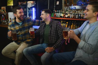 Friends having fun. Happy young men in casual wear drinking beer in pub